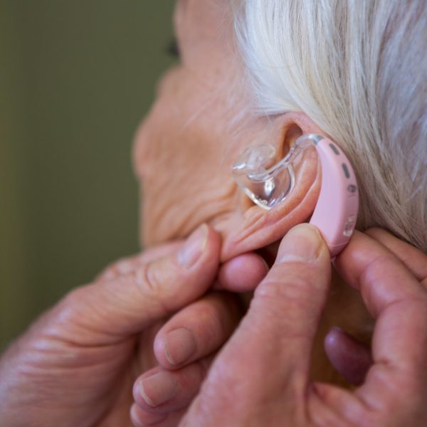 Doctor inserting hearing aid in senior patient ear