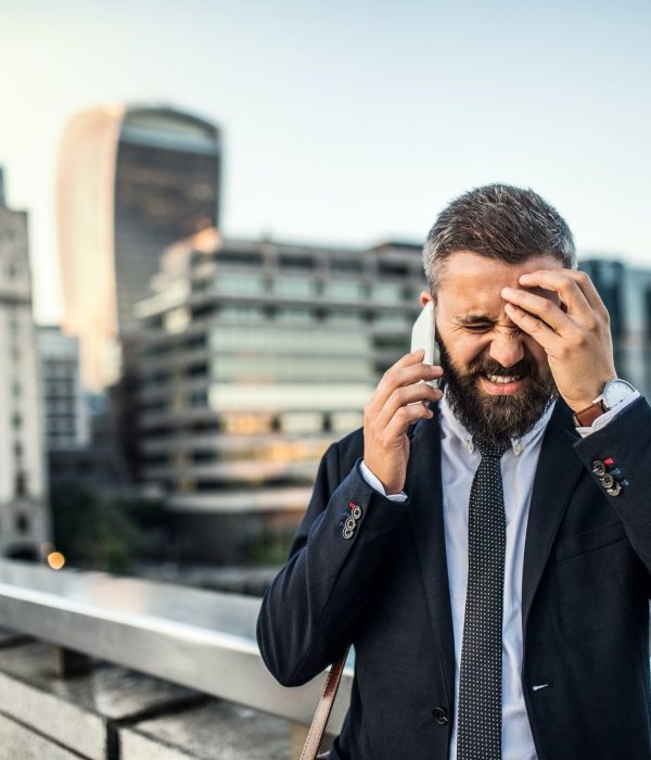 Frustrated hipster businessman with smartphone in the city, making a phone call.